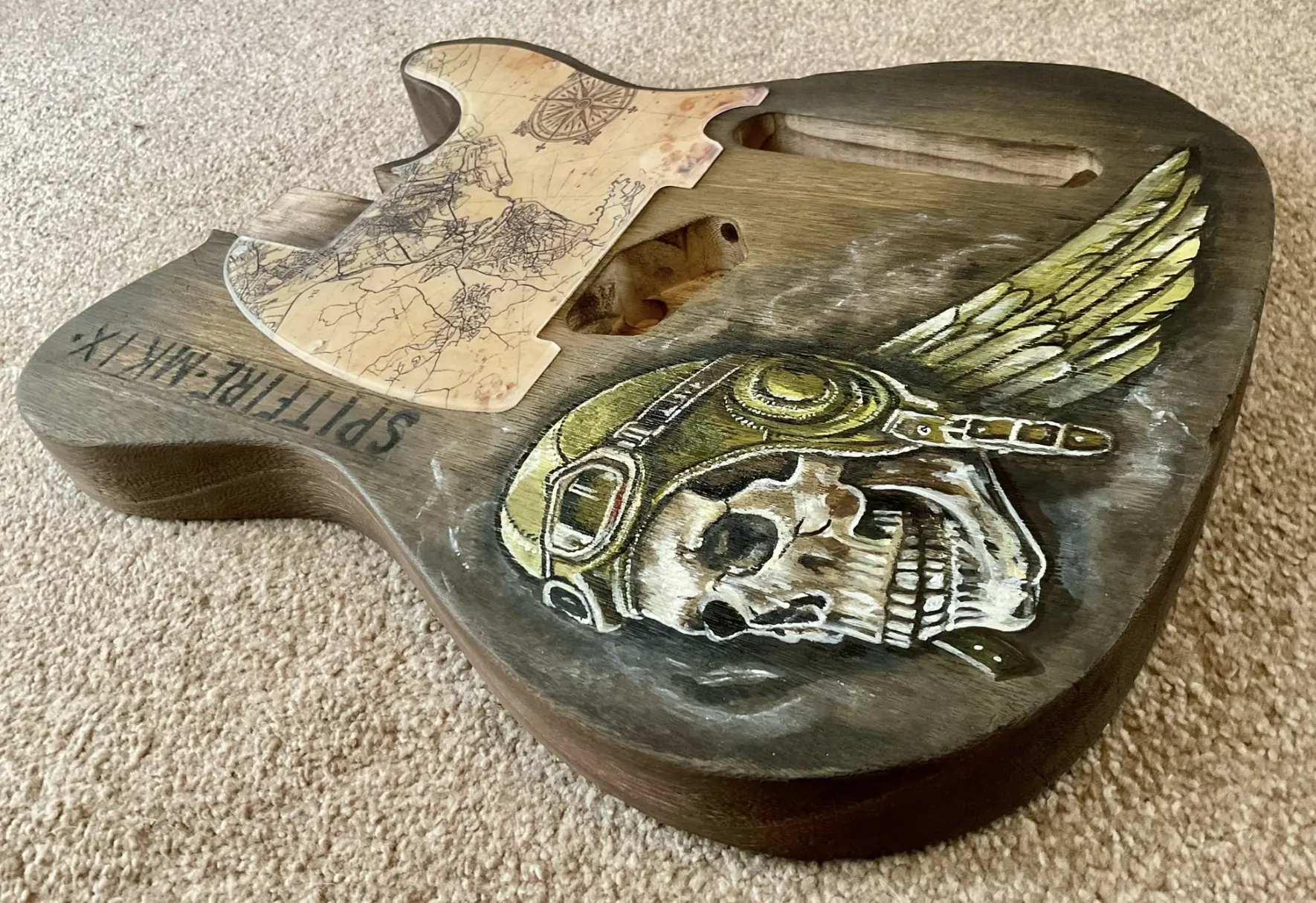 Angled view of a hand-finished T-style guitar body with a map pickguard and aviator artwork